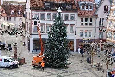 Zwei Bauhofmitarbeiter setzen den Stern auf den großen Weihnachtsbaum auf dem Marktplatz